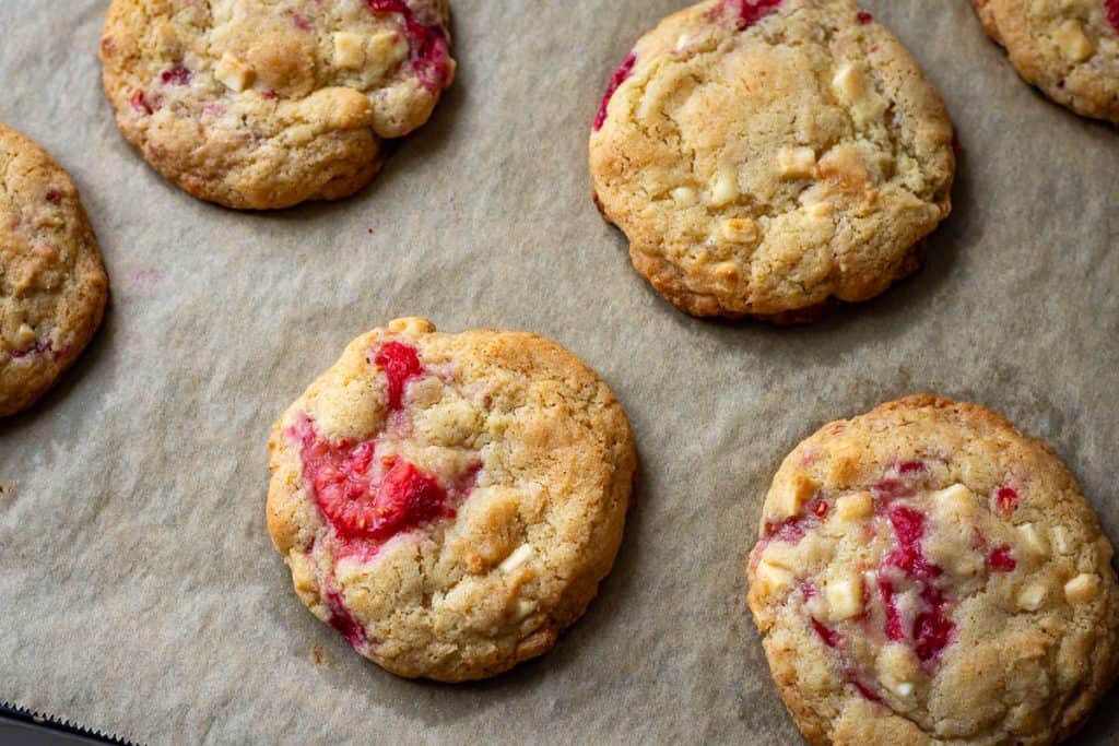 Sunkedn down, crackly topped sourdough cookies with raspberries and white chocolate after dropping the tray on the worktop.