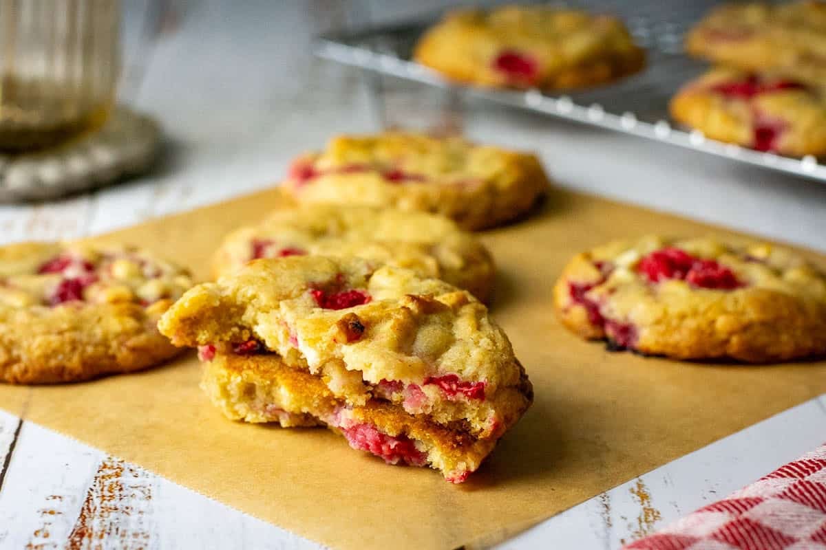 Raspberry and White chocolate sourdough cookie broken in half on a piece of parchment paper.