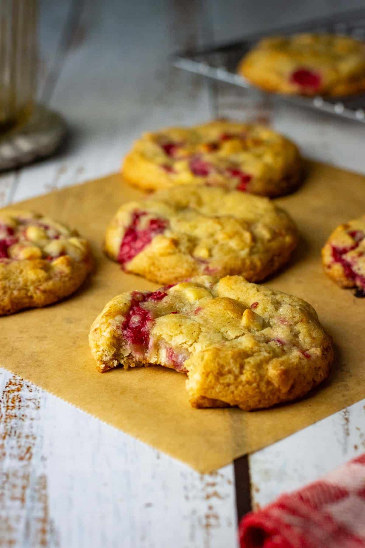 Sourdough Raspberry White chocolate cookies on a parchment paper sheet with one sourdough cookie already missing a bite.