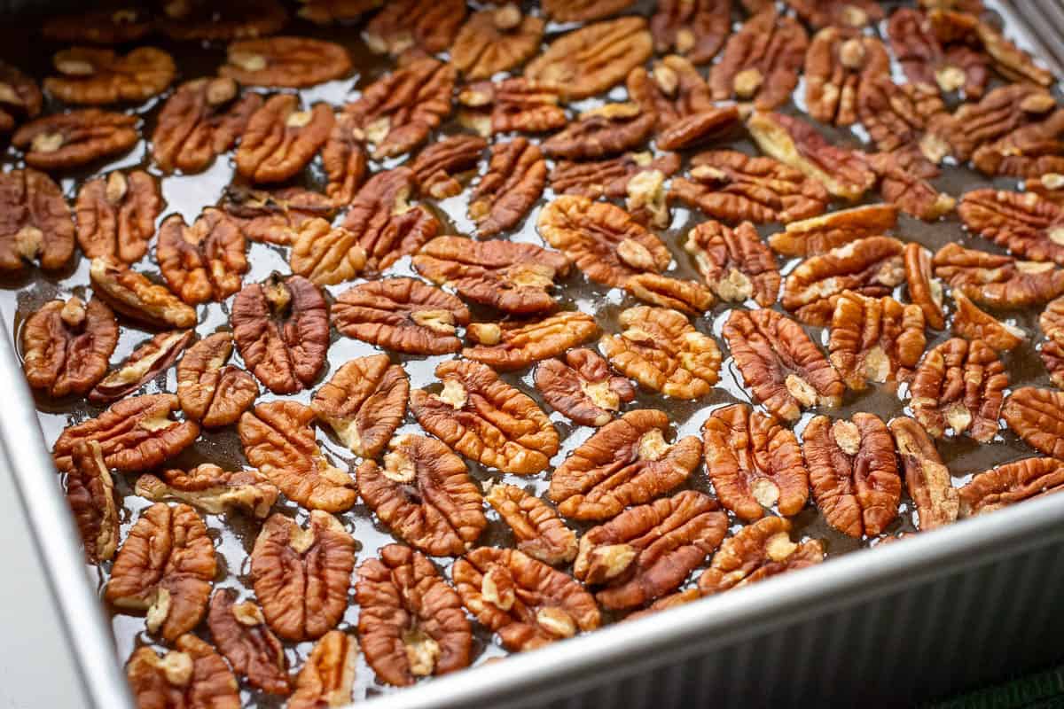 Pecans arranged in a single layer of the caramel on the base of a square baking pan.