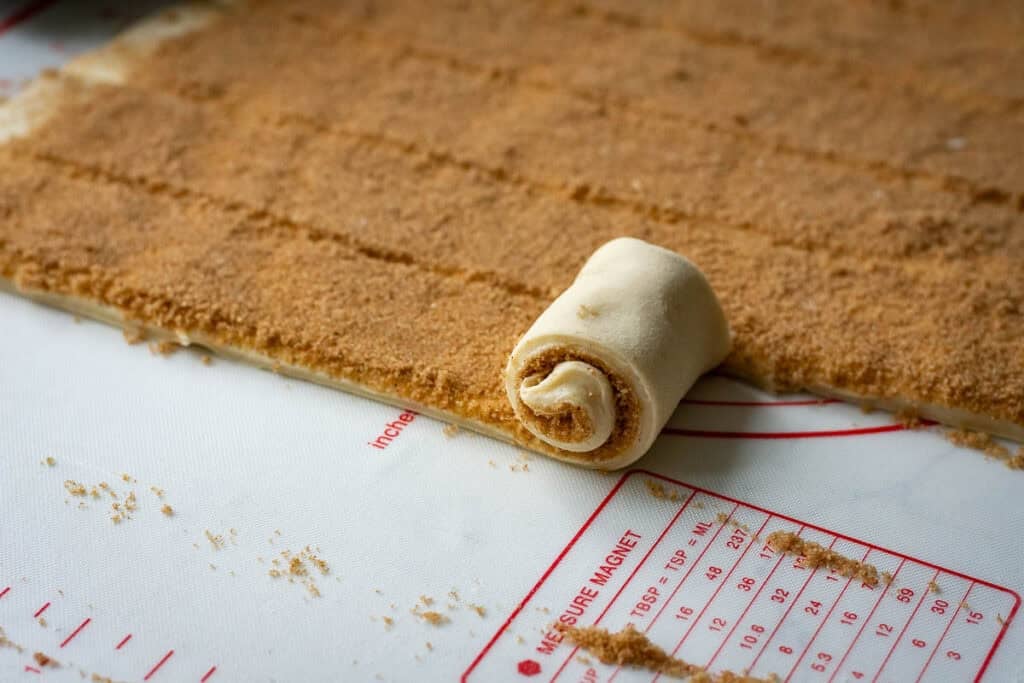 Rolling thin strips of cinnamon sugar filled sourdough into tight rolls.