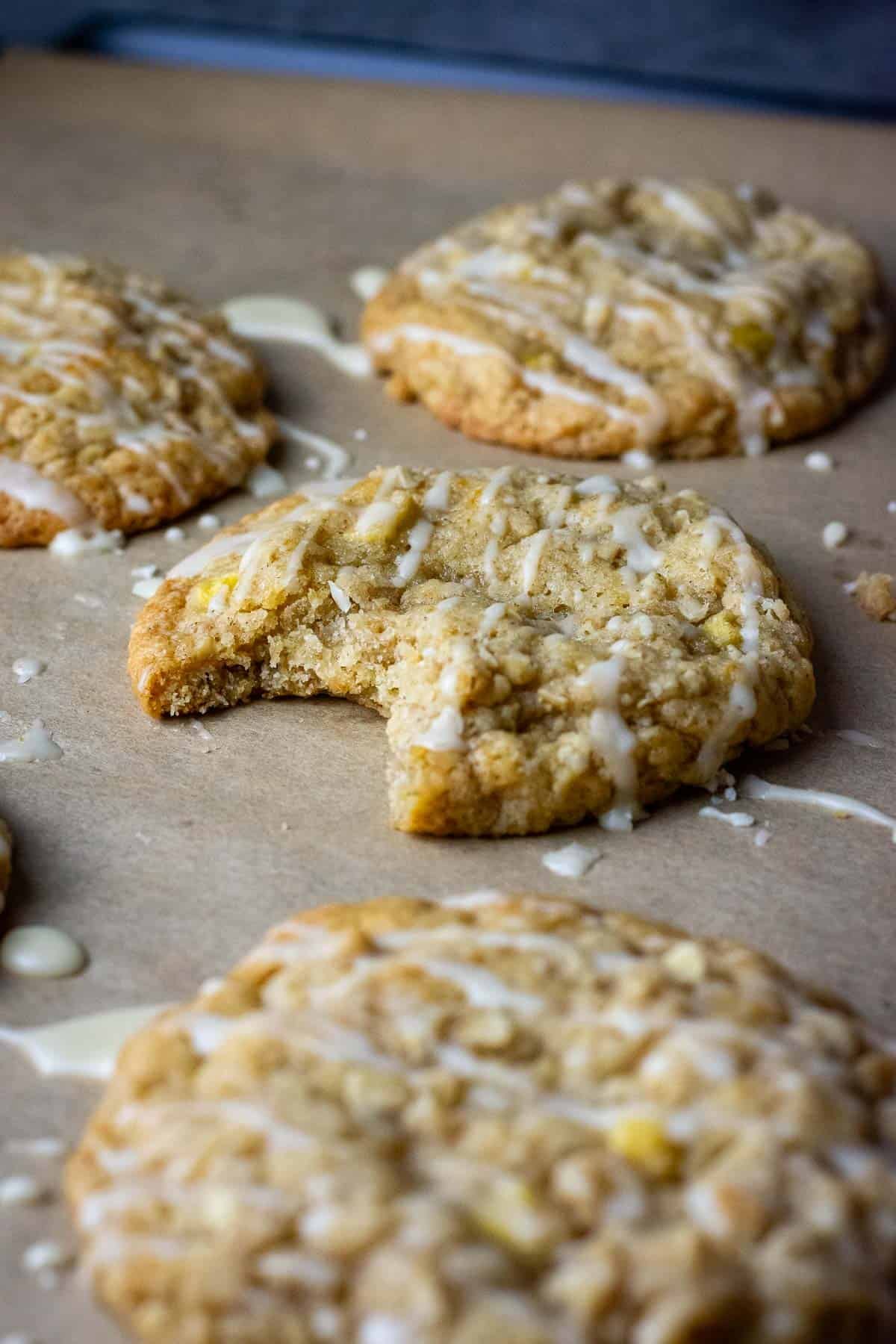 Sourdough apple cookies on a baking sheet lined with parchment paper, one of the cookies bitten into.