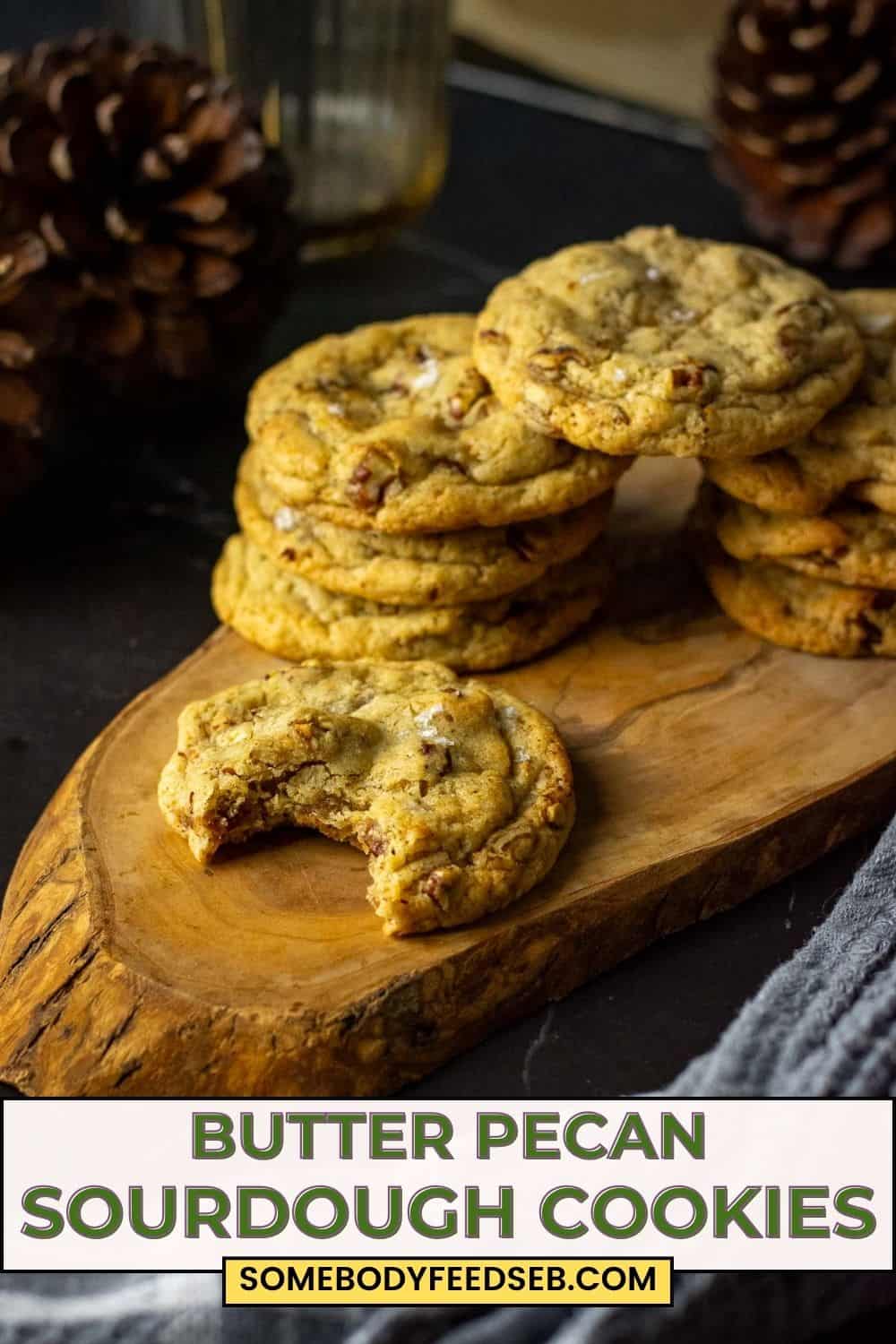 Stacks of butter pacan sourdough cookies on a decorative wooden board with one sourdough cookie already bitten into. Pin for Pinterest.