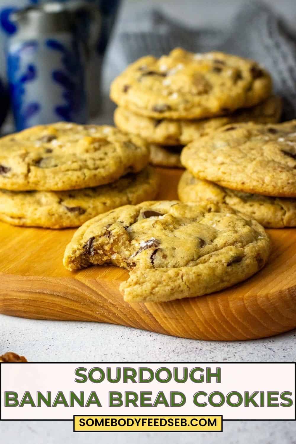 Stacks of sourdough banana bread cookies on a wooden board with one sourdough cookie bitten into. Pin for Pinterest.