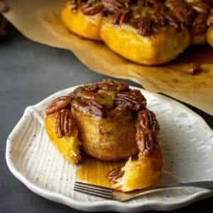 Sourdough Sticky buns wih one of the maple pecan rolls torn off and placed on a white plate.