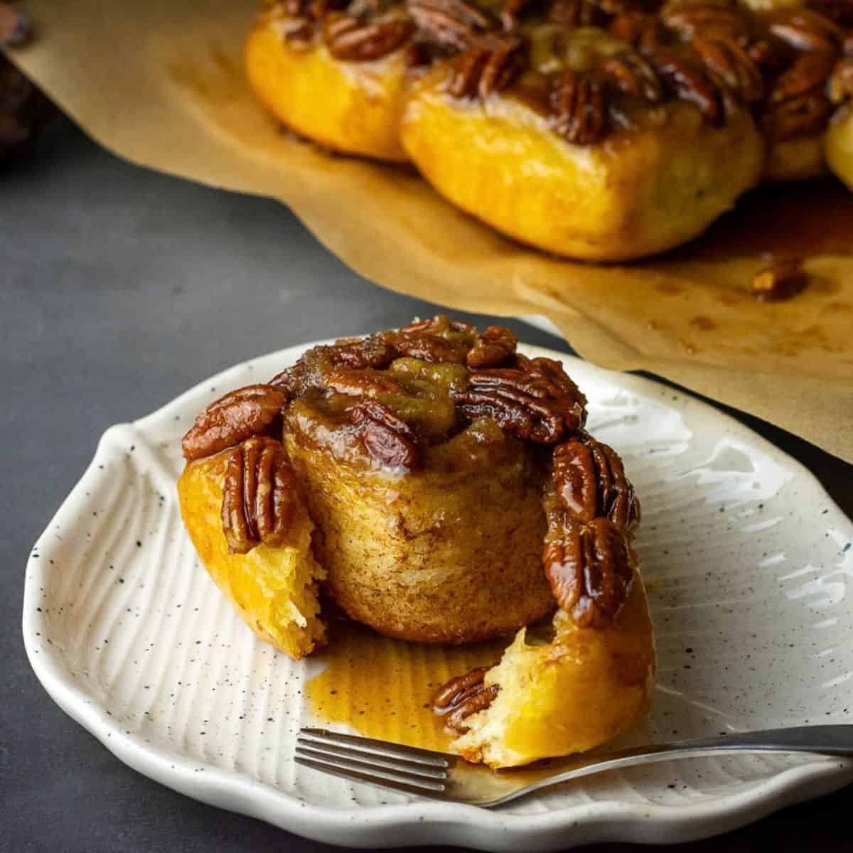 Sourdough Sticky buns wih one of the maple pecan rolls torn off and placed on a white plate.