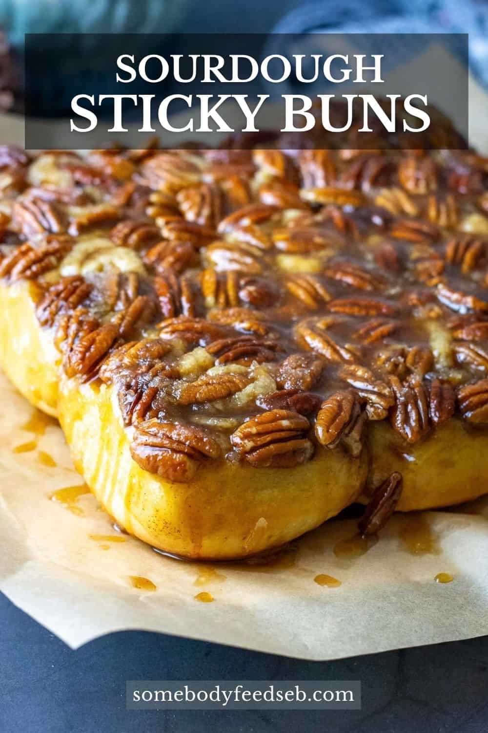 A batch of 9 sourdough sticky buns on a piece of parchment paper with maple pecan caramel dripping down the sides. Pin for Pinterest.