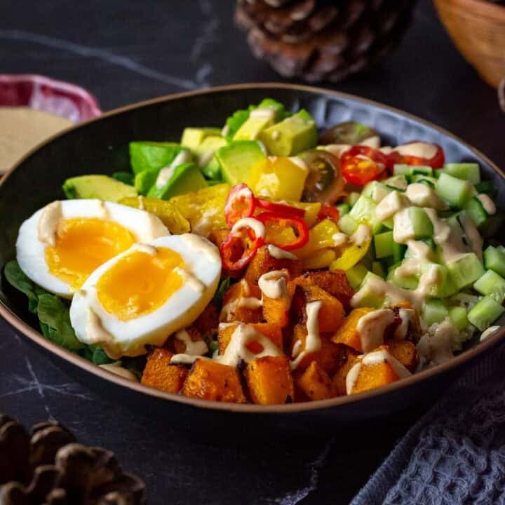 Roasted Butternut Squash Buddha Bowls With Soft Boiled egg and tahini drizzle in a black bowl.