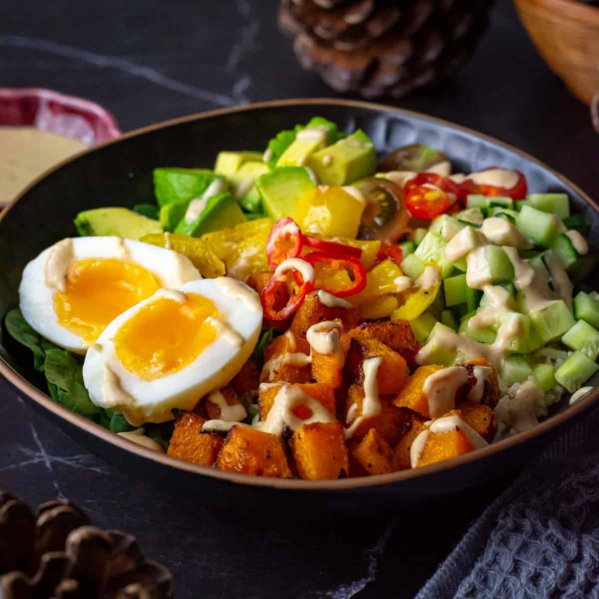 Roasted Butternut Squash Buddha Bowls With Soft Boiled egg and tahini drizzle in a black bowl.