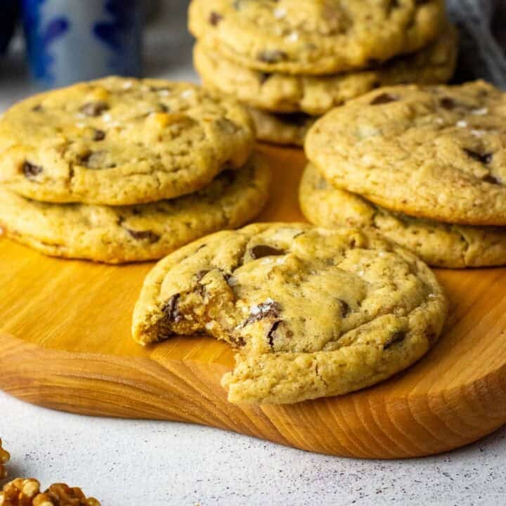 Stacks of sourdough banana bread cookies on a wooden board with one sourdough cookie bitten into.