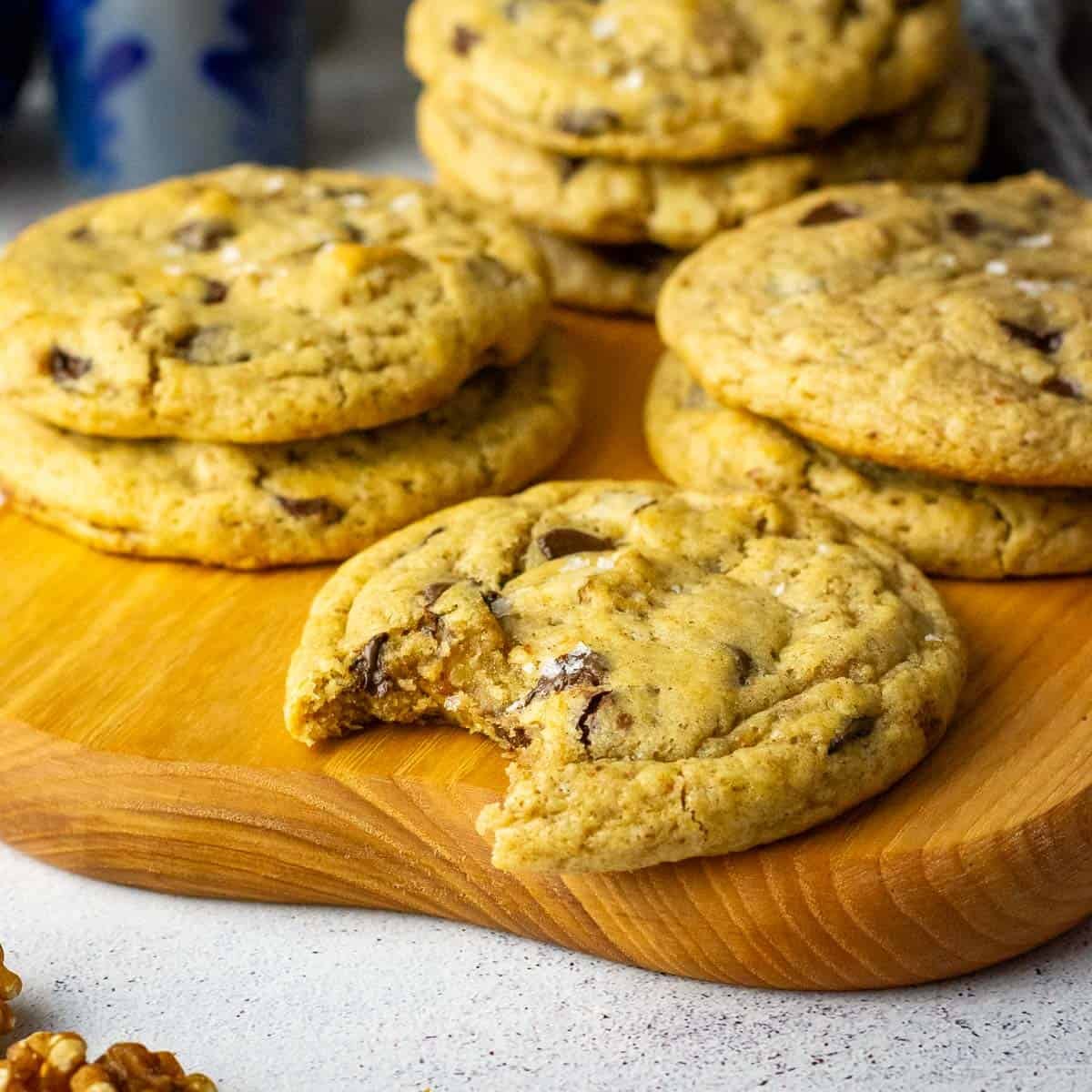 Stacks of sourdough banana bread cookies on a wooden board with one sourdough cookie bitten into.
