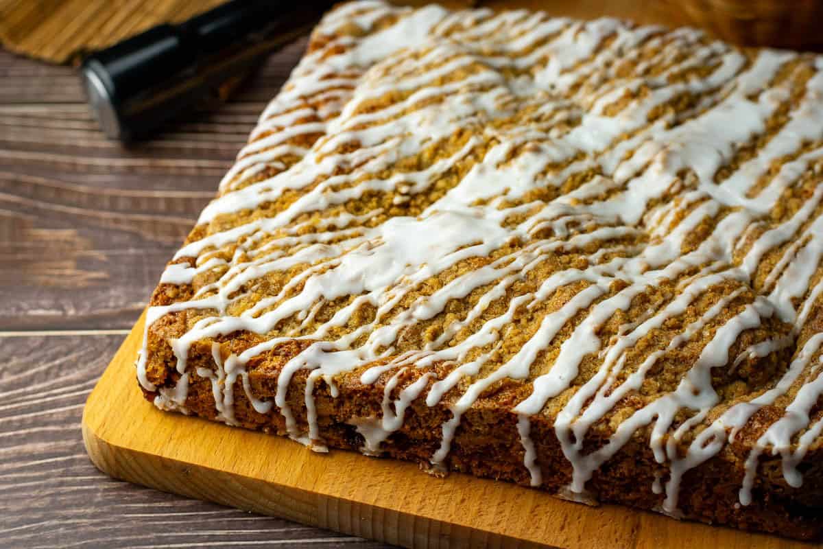 Icing drizzled all over the sourdough coffee cake set on a wooden board for slicing.
