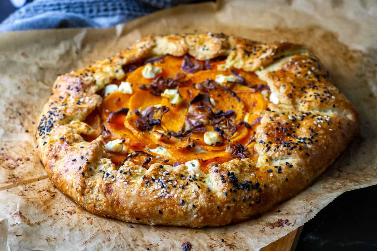 Baked, golden brown sourdough galette with butternut squash, red onion and goat cheese filling on a piece of parchment paper.