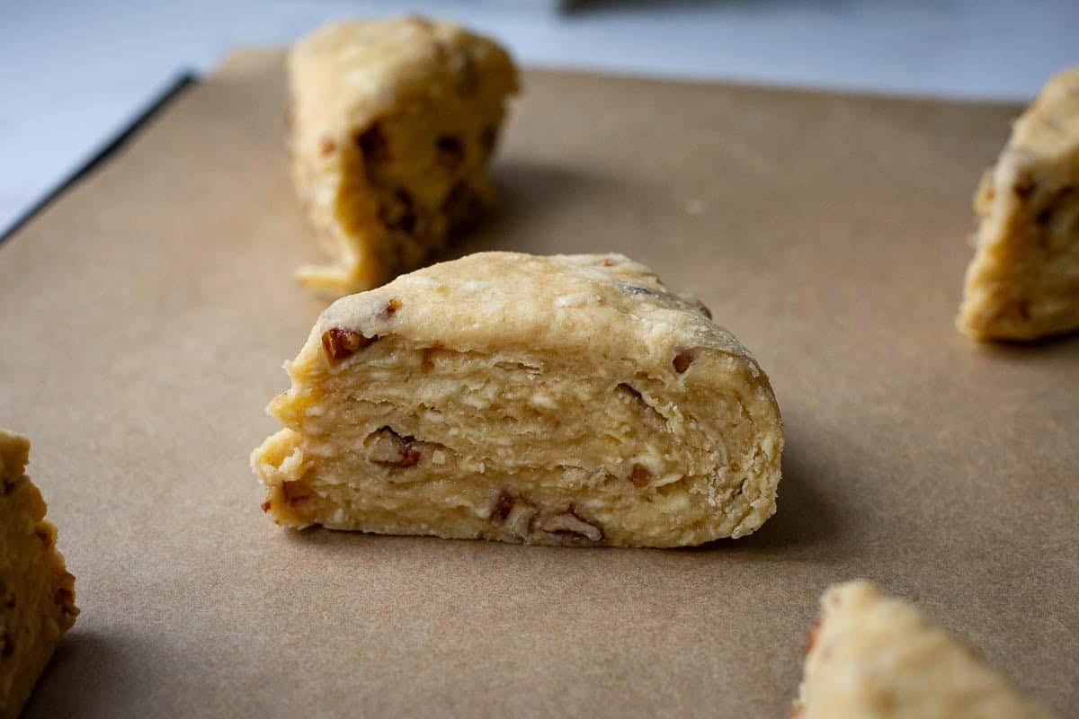 Unbaked maple pecan sourdough scones on a parchment paper lined baking sheet showing clear lamination.