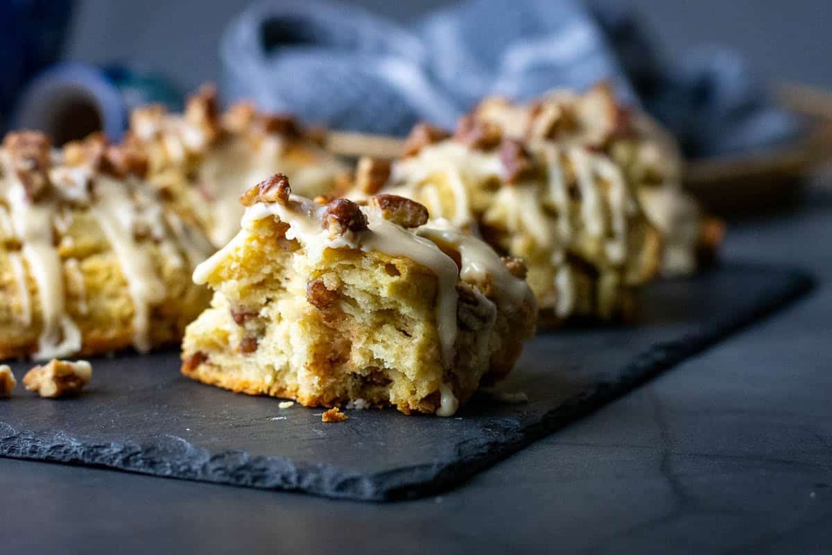 Candied Maple Pecan Sourdough Scones with salted maple glaze and candied pecans on top on a black slate board with one scone missing a half.