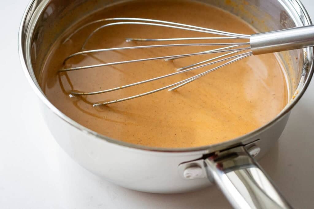 A balloon whisk in a milk and pumpkin mixture left to cool down in a pan.