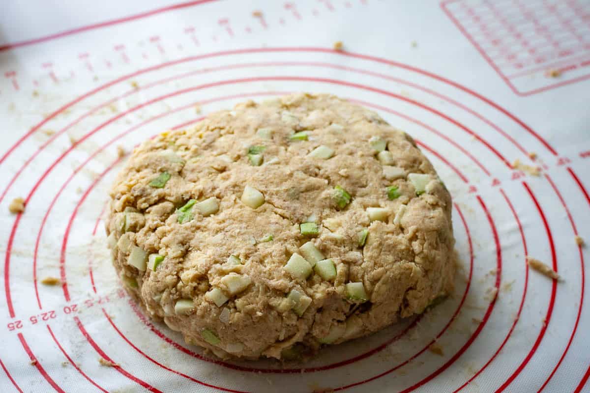 Sourdough scone dough with apple pieces shaped into a disk.