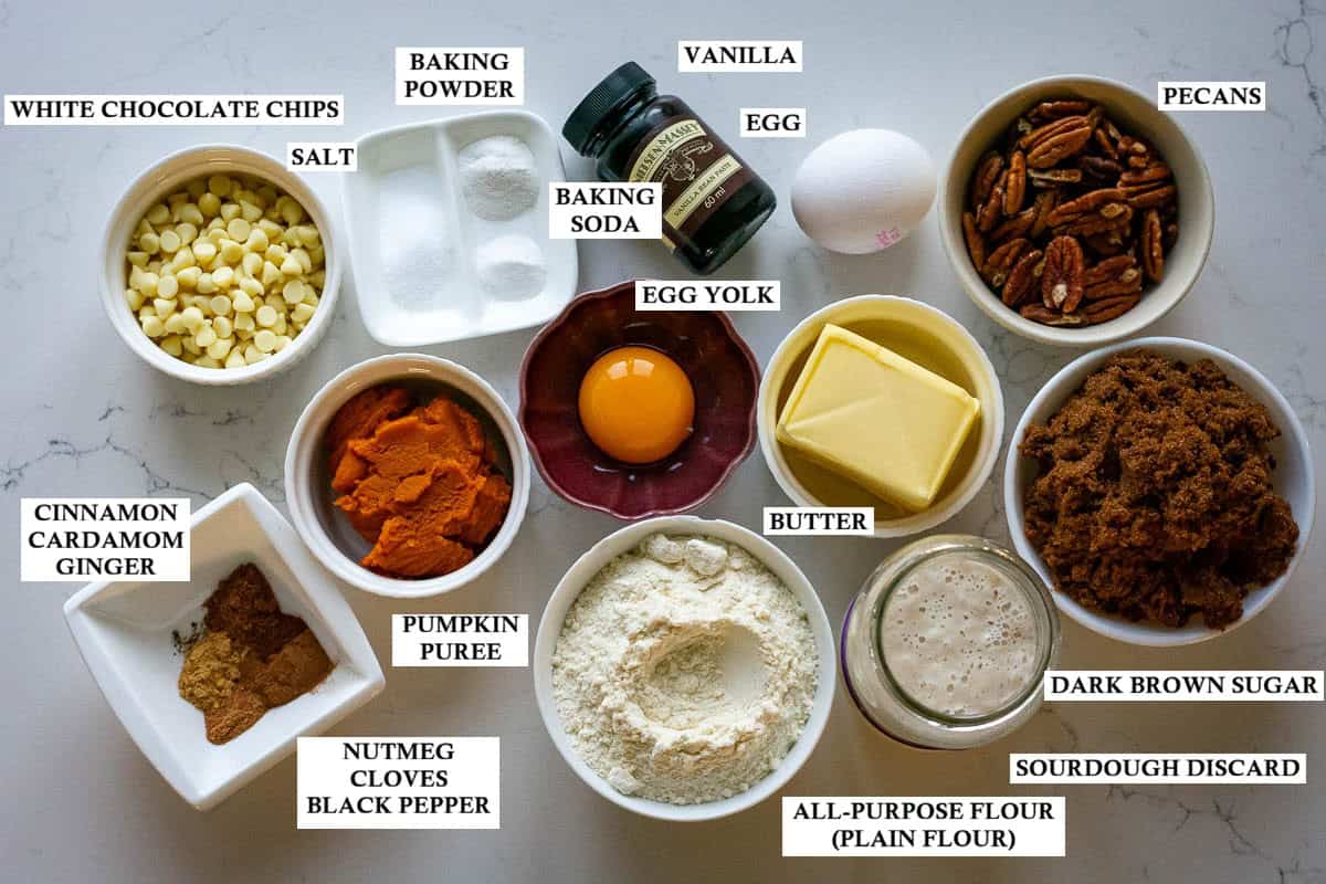 Labelled ingredients for sourdough pumpkin brownies with pecans and white chocolate on a light kitchen worktop.