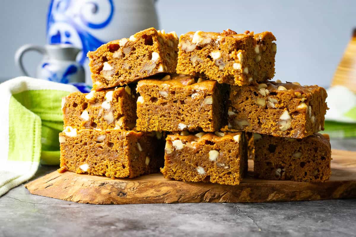A stack of white chocolate and pecan sourdough pumpkin blondies on a decorative wooden board.