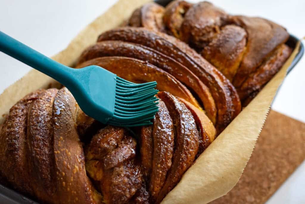 Brushing sugar syrup over the surface of pumpkin sourdough babka.