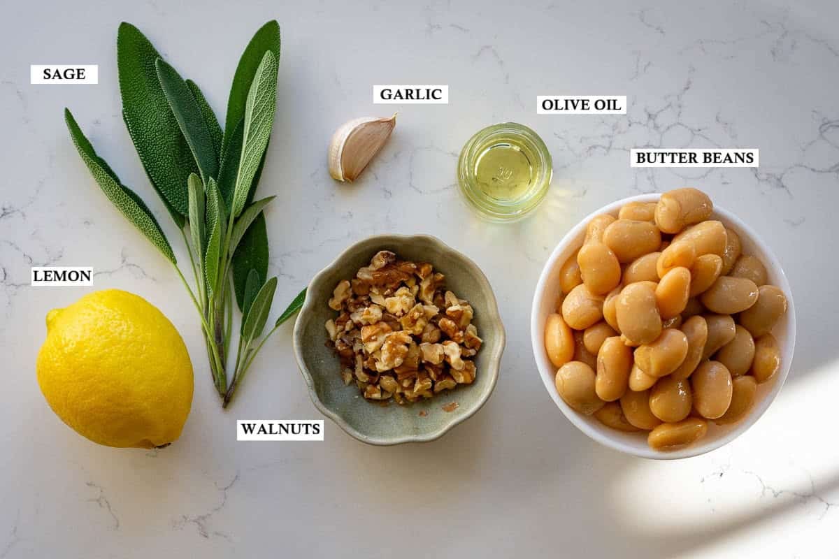 Labelled ingredients for creamy butter bean dip with sage on a light kitchen worktop.