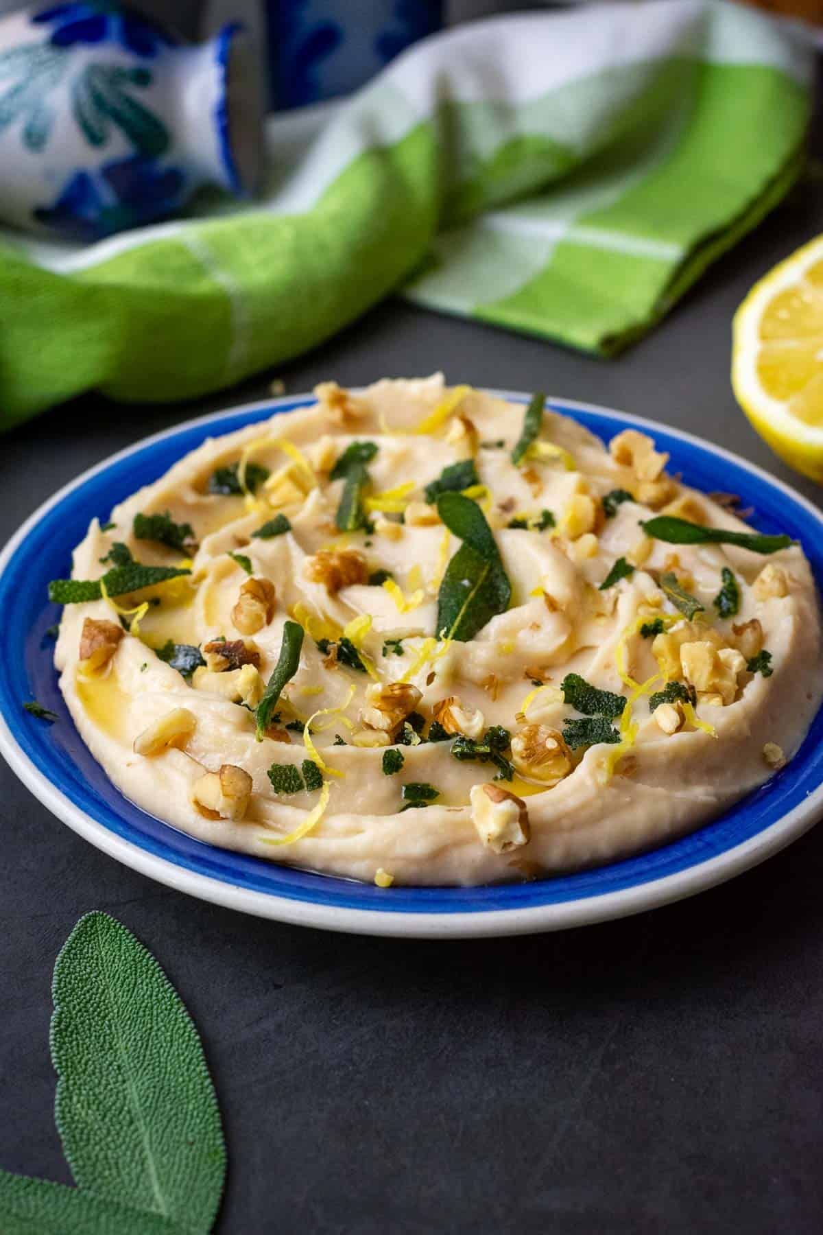 Butter bean dip with grispy sgae and toasted walnuts on top on a blue plate.