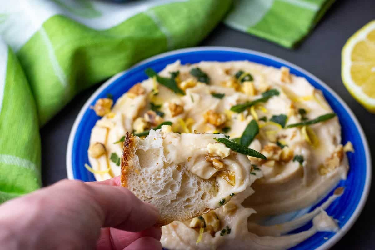 Scooping up some of the creamy butter bean hummum with a piece of sourdough bread.
