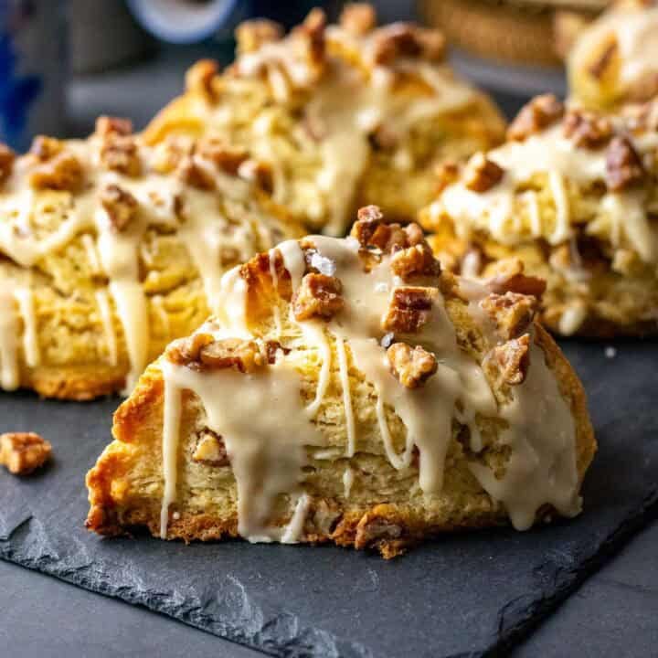 Candied Maple Pecan Sourdough Scones with salted maple glaze and candied pecans on top on a black slate board.