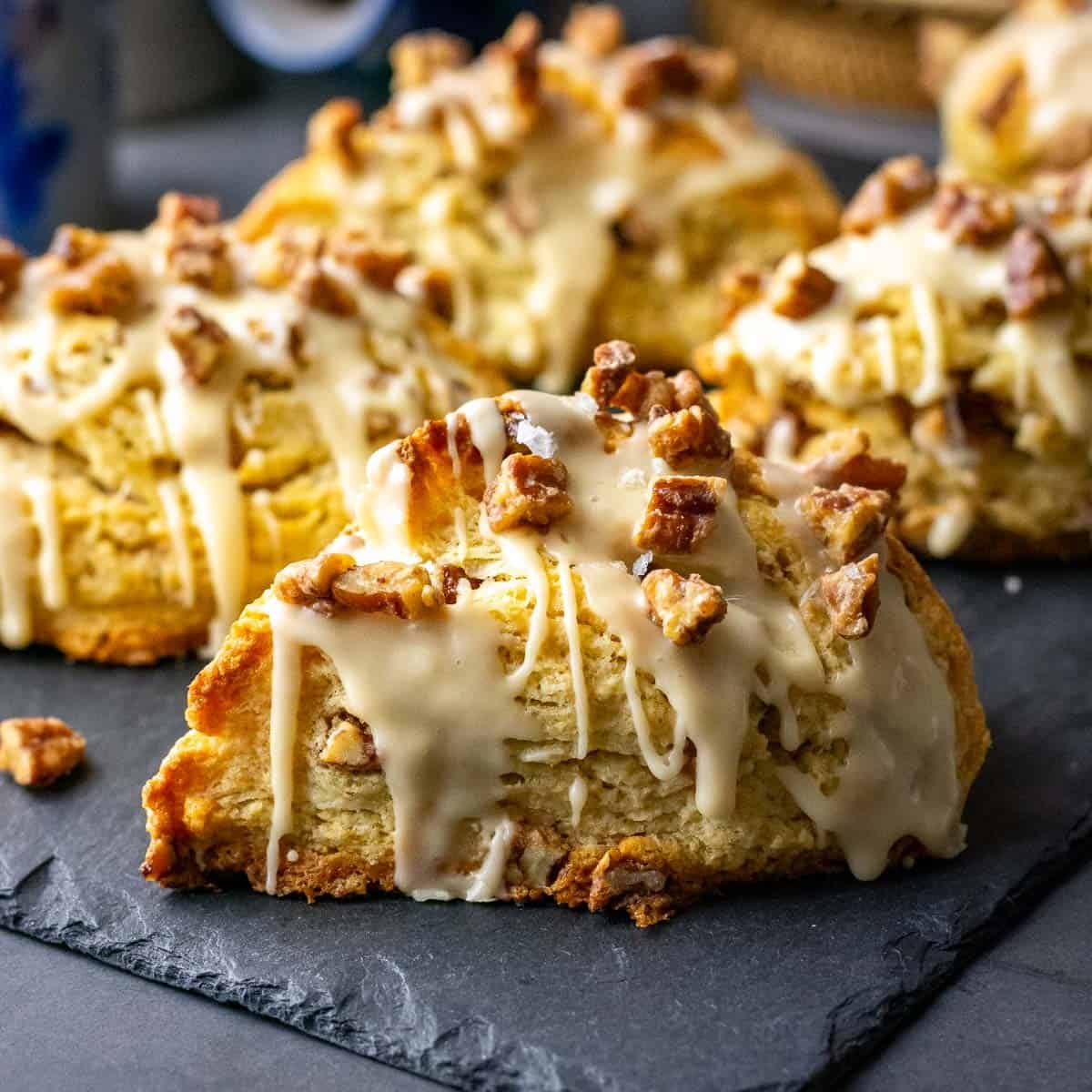 Candied Maple Pecan Sourdough Scones with salted maple glaze and candied pecans on top on a black slate board.