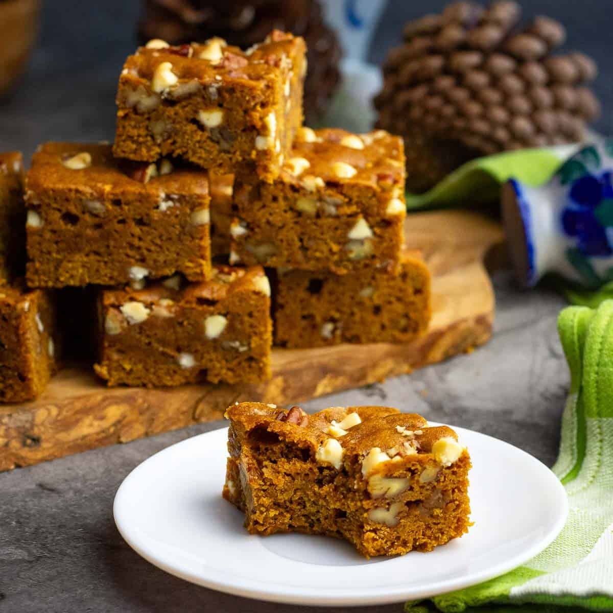 A sourdough pumpkin blondie square bitten into on a small white plate with a stack of sourdough pumpkin blondies in the background.