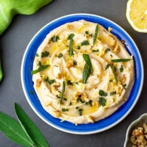 Butter bean dip with crispy sage and toasted walnuts on top on a blue plate.